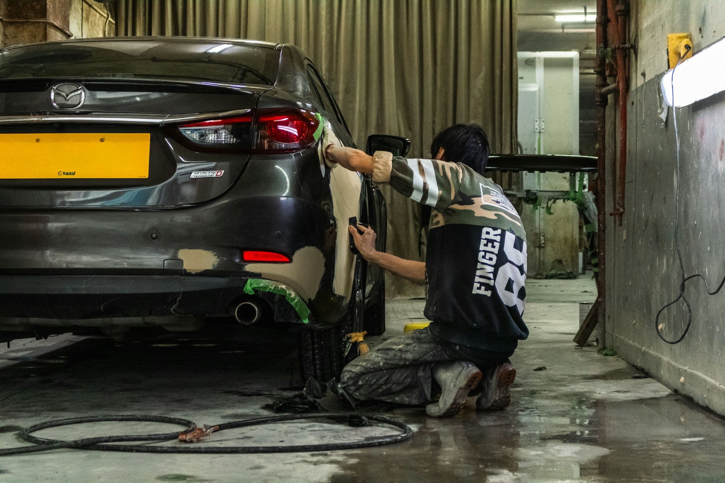 Technician sanding the rear panel of a car in a body shop